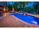 Backyard pool area at dusk, featuring an outdoor fireplace, stone accents, and a view of the lake at 3992 Blue Dory Ln, Denver, NC 28037