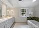 Bright bathroom featuring a double sink vanity, wallpaper, and a soaking tub with decorative tile surround at 2126 Norton Rd, Charlotte, NC 28207