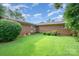 View of the spacious backyard with a brick house, green grass, blue skies and mature landscaping at 812 Clinton Ave, Lancaster, SC 29720