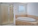 Bright bathroom featuring a glass shower and luxurious soaking tub under a glass block window at 12802 Waterlyn Club Dr, Charlotte, NC 28278