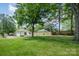 Expansive backyard featuring lush green grass, mature trees, and a charming white house with a wooden fence in the background at 3050 Millstone Dr, Gastonia, NC 28054