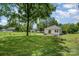 Lush backyard with mature trees, featuring a quaint white house with a concrete patio and manicured lawn in a serene setting at 3050 Millstone Dr, Gastonia, NC 28054