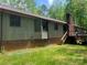 A shot of the rear exterior displaying a brick foundation, wood siding, deck, and mature trees at 1502 Shelby Hwy, Cherryville, NC 28021