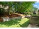 Landscaped backyard featuring artificial turf, mature trees, stone retaining wall, and outdoor seating area at 5818 Downfield Wood Dr, Charlotte, NC 28269