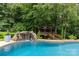 Backyard pool featuring a rock waterfall and a cozy wooden deck nestled amongst mature green trees at 9513 Tresanton Dr, Charlotte, NC 28210