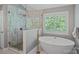 Bright bathroom featuring a free-standing tub, glass-enclosed shower, and a large window with plantation shutters at 1012 Sudbury Ln, Matthews, NC 28104