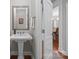 Bathroom with pedestal sink, framed mirror, and an open doorway to dining room with hardwood flooring at 130 Churchill Dr, Salisbury, NC 28144