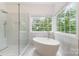 Bright bathroom features a glass shower and a soaking tub with large windows overlooking the wooded yard at 1654 Scotch Pine Ln, Fort Mill, SC 29708