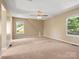 Spacious bedroom with neutral carpet, ceiling fan, and windows overlooking the backyard at 9430 Peckham Rye Rd, Mint Hill, NC 28227