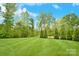 Lush backyard with well-maintained lawn, bordered by mature trees and landscaping with a blue sky overhead at 9596 Pacing Nw Ln, Concord, NC 28027