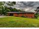 Charming brick home featuring a lush green lawn, mature trees, and an open carport, all under a dramatic sky at 211 Amos Homesley Rd, Cherryville, NC 28021