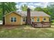 Back exterior of the yellow home with a brick chimney, deck, and well-maintained lawn at 11701 Brockley Ct, Charlotte, NC 28215