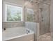Bright bathroom featuring a soaking tub, glass enclosed shower, and neutral tile flooring at 1209 Leigh Ave, Charlotte, NC 28205