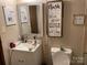 A compact bathroom with a simple vanity, mirror, and toilet, with playful wall decor at 6504 Denver Heights Cir, Denver, NC 28037