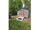Close-up of a storage shed with a red door, set amongst trees in a green yard at 414 Fulton Dr, Kings Mountain, NC 28086