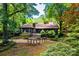 A log cabin nestled among mature trees featuring stone chimney, landscaping, and serene setting at 6510 Sharon Hills Rd, Charlotte, NC 28210