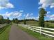 Scenic driveway with white fencing, trees, and a distant view of a house, set under a bright, cloudy sky at 2530 Sharon Rd, York, SC