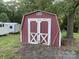 Red storage shed featuring white trim and double doors set in a grassy yard with a few trees at 224 Locust Ave, Locust, NC 28097