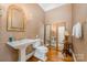 Elegant powder room with a pedestal sink, decorative mirror, wallpaper, and hardwood floors at 5400 Challisford Ln, Charlotte, NC 28226