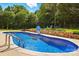 A backyard featuring a blue swimming pool with basketball hoop, surrounded by a stone wall, patio, and green landscaping at 5105 Paisano Ln, Waxhaw, NC 28173
