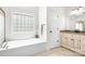 Bright bathroom featuring a soaking tub with tile window, vanity with granite countertop, and neutral tile flooring at 16028 Hallaton Dr, Huntersville, NC 28078