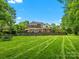 Expansive backyard features a stone retaining wall, manicured lawn, mature trees, and a pool with lounge area at 13029 Whisper Creek Dr, Charlotte, NC 28277