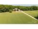 Scenic aerial view of a grand home with a long driveway, set amidst a vast field and surrounded by dense trees at 1720 Mills Harris Rd, Wingate, NC 28174