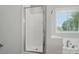 Modern glass-enclosed shower with a white tile surround and window at 8309 Emily Dr, Harrisburg, NC 28075