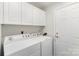 Clean laundry room with a washer, dryer, white cabinets, and a door to an exterior space at 9013 Trellis Pointe Blvd, Charlotte, NC 28227
