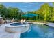 Backyard kidney bean-shaped pool and hot tub, surrounding deck, two blue umbrellas, and wooded surround at 3424 Saint Clair Nw Ct, Concord, NC 28027