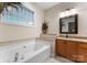 Bright bathroom featuring a large soaking tub, tiled backsplash, granite countertops, and a decorative mirror at 18846 Cloverstone Cir, Cornelius, NC 28031