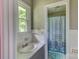 Cozy bathroom featuring a window, sink with a tiled countertop and a charming shower with a patterned curtain at 413 N Mulberry St, Cherryville, NC 28021