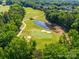 Scenic aerial view of a golf course featuring lush green fairways, a tranquil pond, and mature trees at 7006 Olde Sycamore Dr, Mint Hill, NC 28227