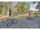 Outdoor picnic tables and umbrellas set on a gravel surface, with grass, trees, and clubhouse in the background at 7600 Ridgefield Dr, Charlotte, NC 28269