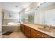 Bright bathroom featuring double sinks with wood cabinetry, a soaking tub, and a large mirror at 10452 Quiet Bay Ct, Charlotte, NC 28278