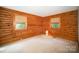 Cozy bedroom with log walls, two windows, neutral carpet, and warm natural light at 8464 Robinson Church Rd, Charlotte, NC 28215