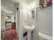 Cozy half-bathroom featuring a pedestal sink, decorative mirror, and a glimpse into an adjacent room at 907 Edgewood Cir, Gastonia, NC 28052