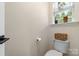 Powder room with window, toilet, neutral wall color, and woven basket shelf at 7341 Adare Mews Rd, Charlotte, NC 28217