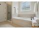 Bright bathroom featuring a shower, large soaking tub, and a window with decorative glass block, creating a spa-like ambiance at 15714 Laurel Oak Cres, Davidson, NC 28036