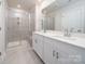 Well-lit bathroom featuring dual sinks, white cabinets, a tiled shower with glass doors, and modern fixtures at 4213 Summit Woods Dr, Charlotte, NC 28216