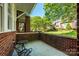 Relaxing covered front porch with brick surround, cozy seating, and a view of the green lawn and landscaping at 6312 Mission Pl, Charlotte, NC 28210