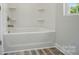White tub and shower combination with built-in shelves, gray wood-look flooring, and a window for natural light at 910 Westminster Dr, Statesville, NC 28677