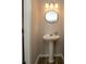 Neutral toned half bath with hardwood floors, pedestal sink, round mirror and three-bulb vanity light at 4938 Sunset Ridge Ct, Charlotte, NC 28269