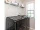 Convenient laundry room featuring modern gray front loading washer and dryer, with shelving and natural light at 8317 Dallas Bay Rd, Charlotte, NC 28278