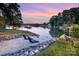 Beautiful waterfront with a sandy beach area, lounge chairs, and lush greenery at twilight at 108 Balmoral Dr, Mooresville, NC 28117
