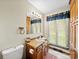 Traditional bathroom with wood cabinets, large mirror, and natural light from the window with blue curtains at 40278 Nc 740 Hwy, New London, NC 28127