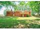 Exterior shot of a brick home's backyard featuring a wooden balcony, lush green lawn, and mature trees at 619 E Sanders Rd, Shelby, NC 28150