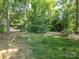 A view of the level, grassy backyard surrounded by mature trees at 2222 Hearthstone Dr, Gastonia, NC 28056