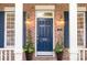 Close-up of a classic blue front door with decorative lanterns and potted plants, framed by brick and white columns at 239 N Faulkner Way, Davidson, NC 28036