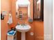 Stylish half bathroom with pedestal sink, hexagon mirror, and unique orange walls at 9718 Eagle Feathers Dr, Charlotte, NC 28214